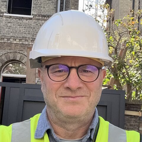 Duncan Gilbert in a hard hat and hi-vis vest outside a Victorian house under retrofit